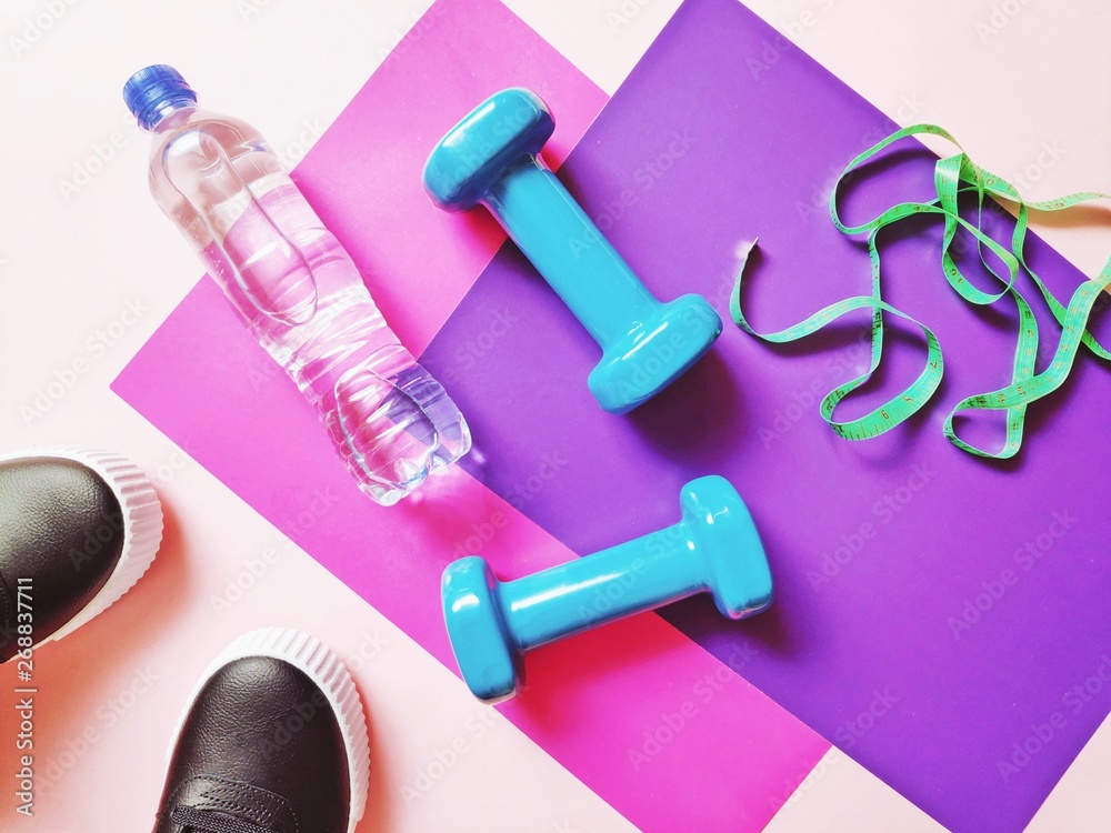 Flat lay photo sneakers, plastic bottle of water, blue dumbbells and measuring tape on a pink and purple background. Fitness, healthy lifestyle concept Flat lay photo sneakers, plastic bottle of water, blue dumbbells and measuring tape on a pink and purple background. Fitness, healthy lifestyle concept