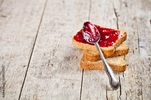 Quadro su tela Toasted cereal bread slices stack with homemade cherry jam and spoon closeup on rustic wooden table background