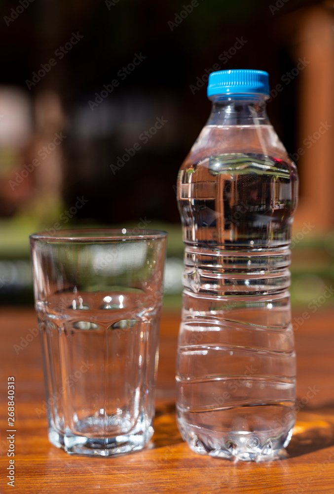 Full of fresh drinking water in plastic bottle and a glass of water on brown wooden table