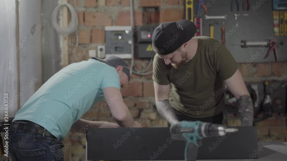 Two guys working in a small workshop with tools. Two woodworkers craft wood pieces with her tools. Concept of hand manufacturing. Craftman works in a workshop. Two guys working in a small workshop with tools. Two woodworkers craft wood pieces with her tools. Concept of hand manufacturing. Craftman works in a workshop.