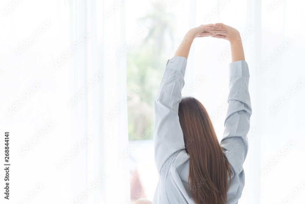 Young beauty asian woman wake up and stretching oneself looking outside window from bedroom