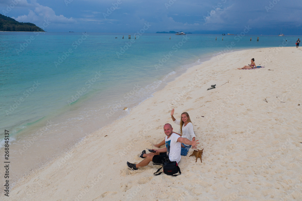 Aerial drone view of happy couple with dog sitting on the sandy white beach over lagoon sea and sky background Aerial drone view of happy couple with dog sitting on the sandy white beach over lagoon sea and sky background