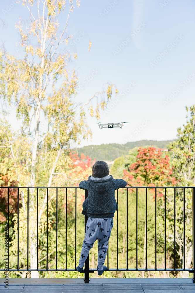 Child watching a drone flying from a balcony Child watching a drone flying from a balcony