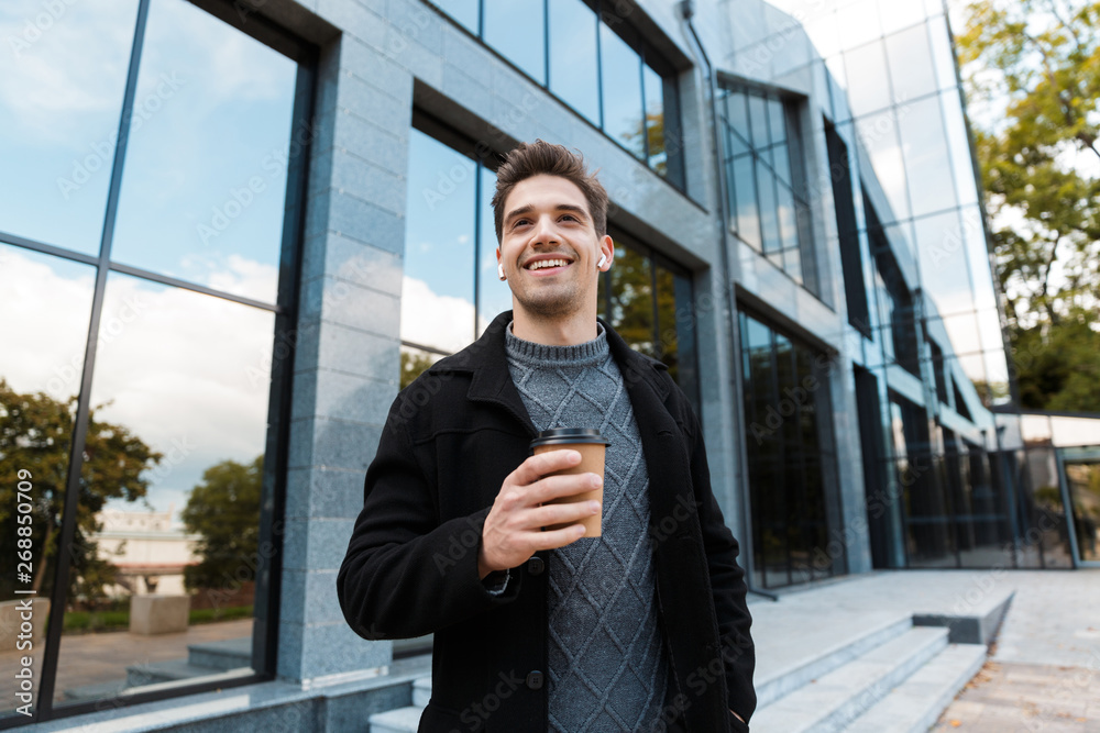 Portrait of handsome man holding paper cup of takeaway coffee while strolling in front of glass building Portrait of handsome man holding paper cup of takeaway coffee while strolling in front of glass building