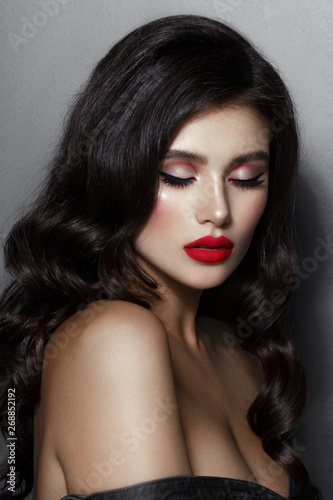 Closeup portrait of a brunette female model with makeup  closed eyes  hair and red lips  isolated on gray background.