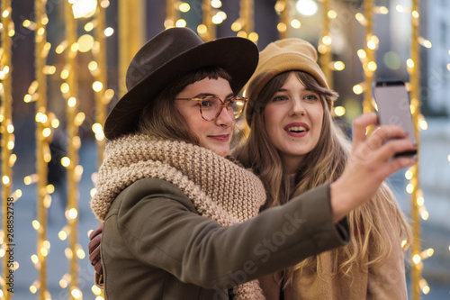 Two Young Women Taking A Photo With A Phone On The Christmas Eve