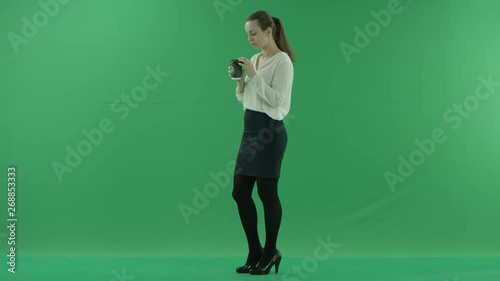 business woman is drinking a cup of coffee or tea. She wears formal dress: white shirt and blak skirt. Businesswoman think, got idea and smile sideways over green screen photo