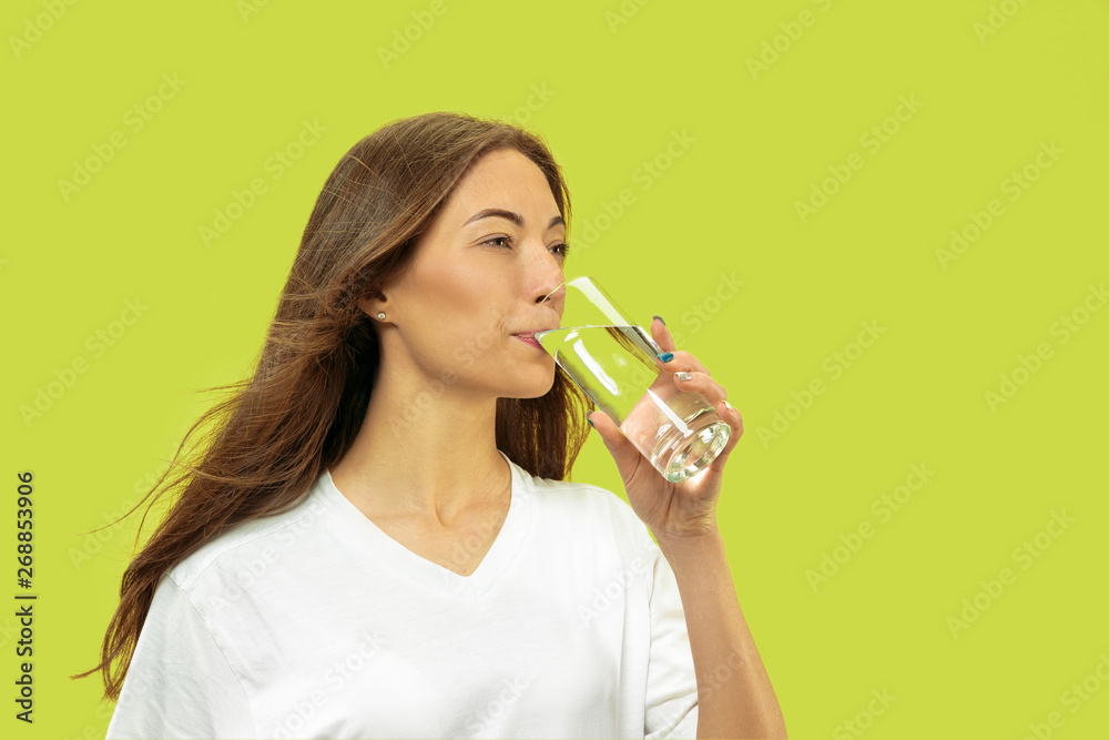 Beautiful young woman's half-length portrait isolated on green studio background. Female model looks happy and drinking water. Facial expression, human emotions concept, beauty and healthcare. Beautiful young woman's half-length portrait isolated on green studio background. Female model looks happy and drinking water. Facial expression, human emotions concept, beauty and healthcare.