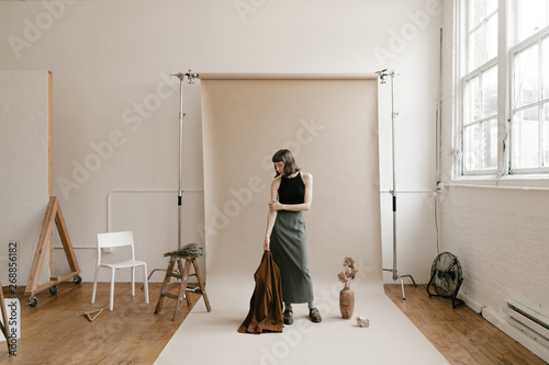 behind the scenes of model standing on backdrop paper in photo studio with props around photo