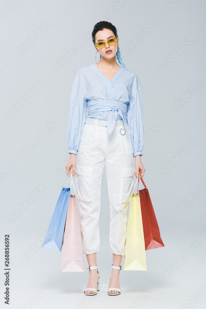 beautiful fashionable girl with shopping bags looking at camera on grey