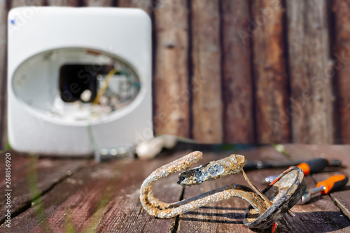 Heating element, rust and scale on boiler background, lying on wooden table. Wooden wall on the background photo