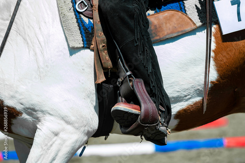 cowboy leg in a stirrup riding a paint horse detail close up
