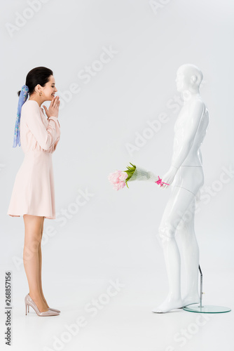 beautiful excited girl and mannequin with flower bouquet isolated on grey