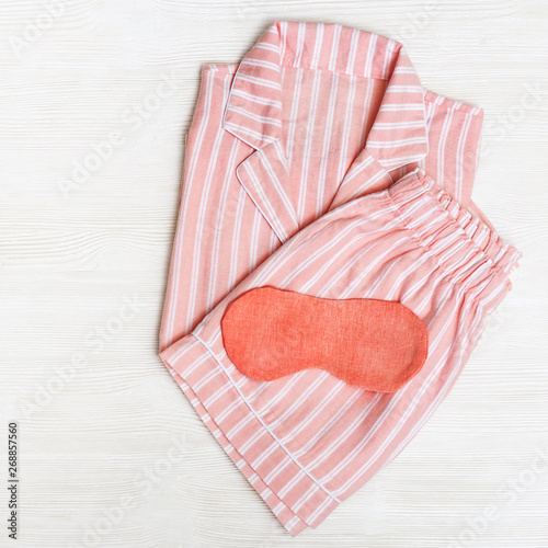 Sleepwear for slumber. Pink womens pajamas with stripes, shirt and shorts.  Sleeping mask on white sheet. copy space. Top view. Flat lay.