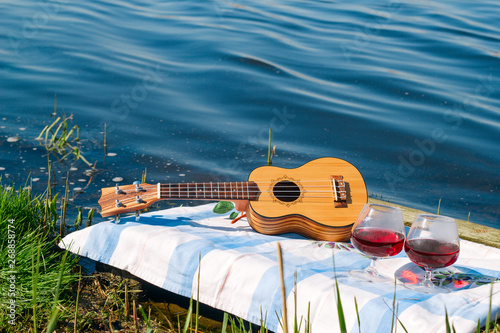 hawaiian guitar and two red wine glasses, picnic on the lake and summer vacation concept photo