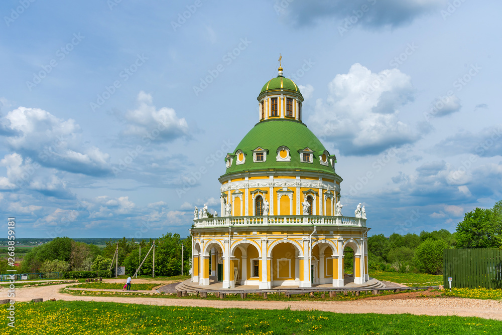 Church of the Nativity of the Virgin in Podmoklovo, Russia. Spring day with a dramatic sky. Flowering dandelions.