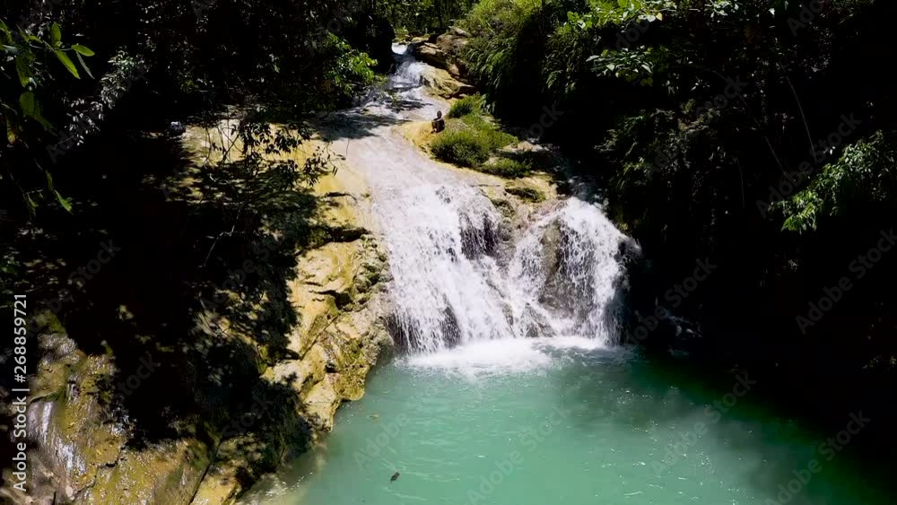 Shaded jungle waterfall running from elevated creek cascading into tranquil sun lit turquoise pool below. Shaded jungle waterfall running from elevated creek cascading into tranquil sun lit turquoise pool below.