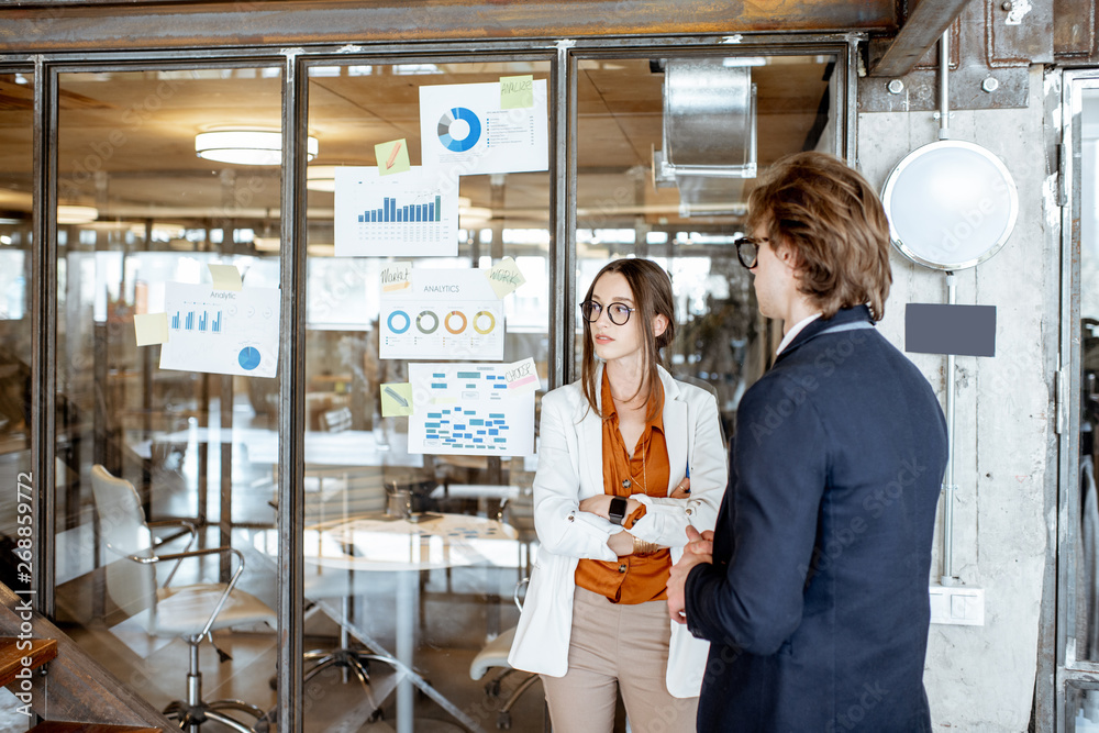 Business people having a discussion while working with charts and drawings on the glass wall in the office Business people having a discussion while working with charts and drawings on the glass wall in the office