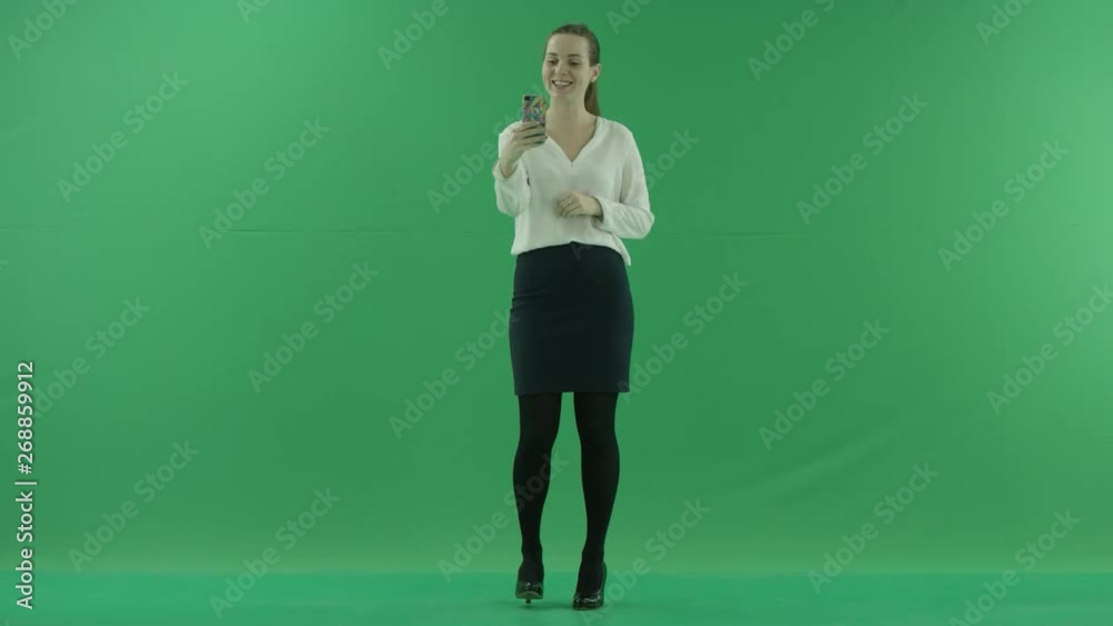 Excited young business woman is having online video chat. She wears formal dress: white shirt and blak skirtand stands on the green screen. Excited young business woman is having online video chat. She wears formal dress: white shirt and blak skirtand stands on the green screen.