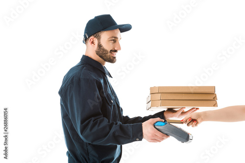 partial view of female hand with credit card near cheerful delivery man holding payment terminal and pizza boxes isolated on white