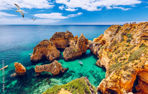 Panoramic view, Ponta da Piedade with seagulls flying over rocks near Lagos in Algarve, Portugal. Cliff rocks, seagulls and tourist boat on sea at Ponta da Piedade, Algarve region, Portugal. photo