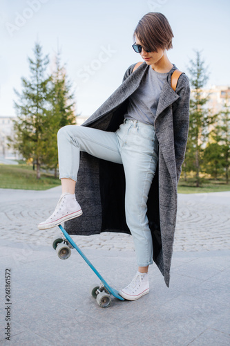 Beautiful young woman in fashonable clothes is stroll skating in the city park photo