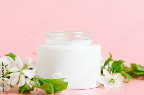 Face cream in white jar on a pink background with white flowers. Concept natural cosmetics  organic beauty. Copy space.