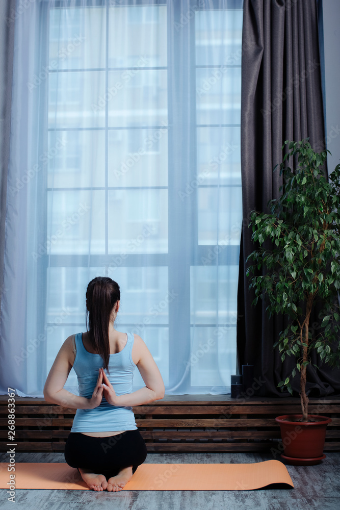 a young girl does yoga on the mat in the studio with her hands folded in a prayer pose with your hands behind your back. soft focus and rear view a young girl does yoga on the mat in the studio with her hands folded in a prayer pose with your hands behind your back. soft focus and rear view