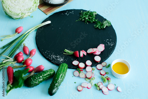 Fresh spring vegetables such as radishes  onions  cucumbers  cabbage and other ingredients are sliced and prepared for a bright  juicy salad on a stone cutting board. top view