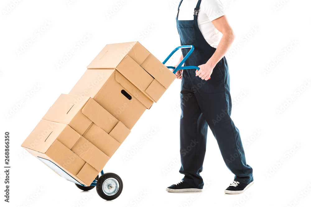 cropped view of delivery man in overalls transporting hand truck loaded with cardboard boxes isolated on white cropped view of delivery man in overalls transporting hand truck loaded with cardboard boxes isolated on white