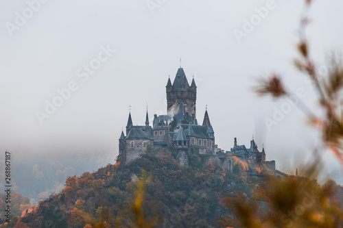 Reichsburg Cochem / Castle Cochem covered in fog during an orange and misty autumn day with low hanging clouds and fog (Cochem, Germany, Europe)