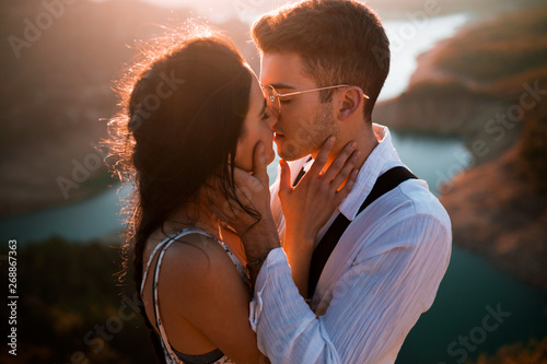 Beautiful young couple in love kissing and touching their faces on the mountain photo