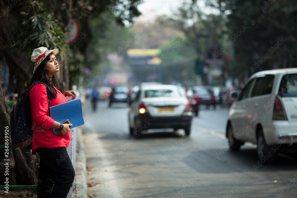 A college girl awaiting by the side of a road in city area