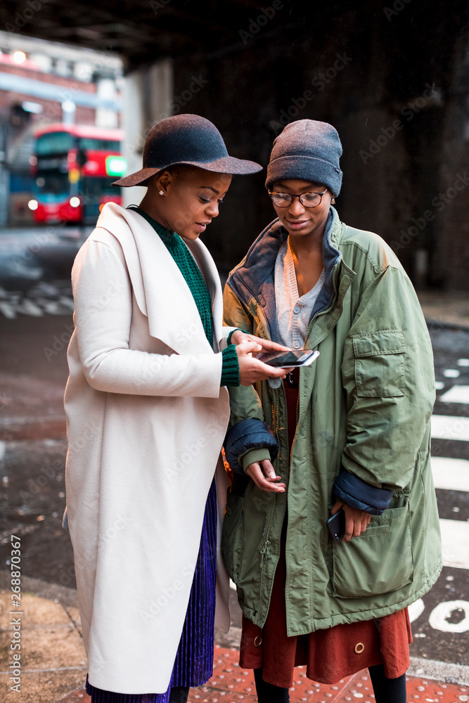 Stylish female friends using mobile phone in London Stylish female friends using mobile phone in London