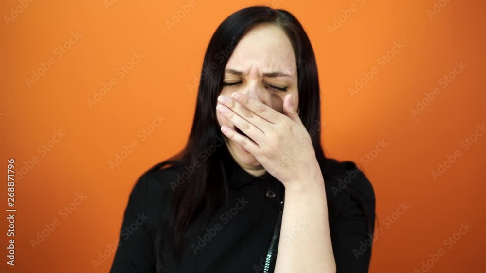 Yawning woman on orange background. Young brunette woman covering her mouth and yawning Yawning woman on orange background. Young brunette woman covering her mouth and yawning