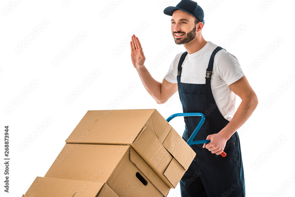 happy delivery man transported cardboard boxes loaded on hand truck and showing hello gesture isolated on white happy delivery man transported cardboard boxes loaded on hand truck and showing hello gesture isolated on white