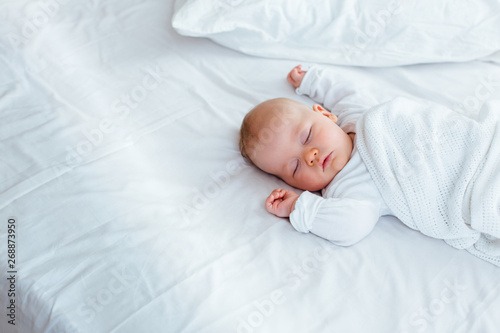 A sleeping baby in a white sleepsuit lysing on a white background