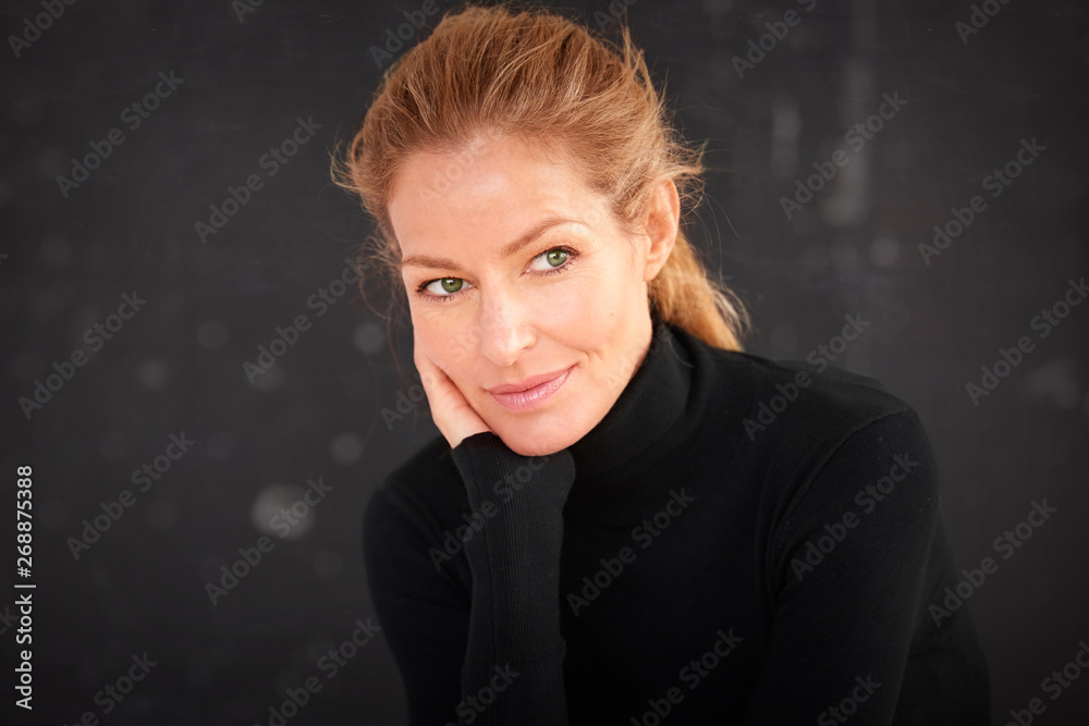 Fototapeta premium Attractive blond haired woman wearing roll neck sweater and thinking while sitting at dark background