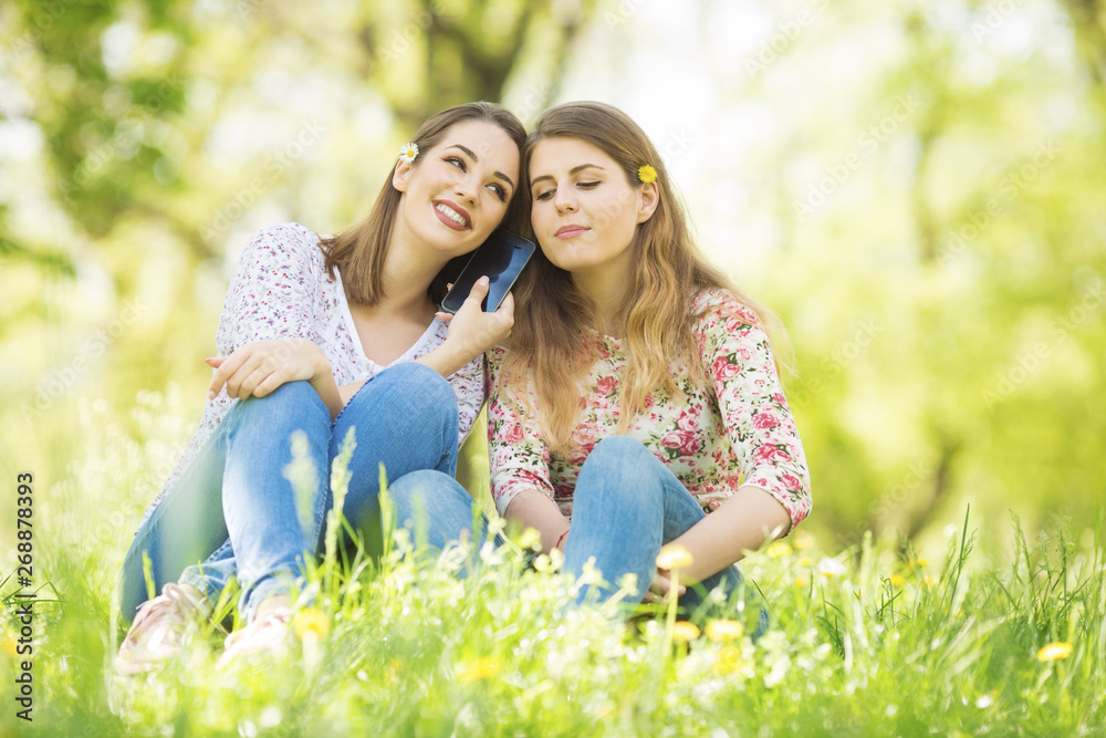 Two young women sitting outdoors and using phone Two young women sitting outdoors and using phone
