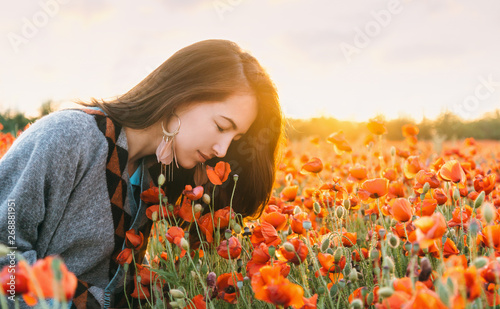 Romantic girl smelling a poppy flower in field.