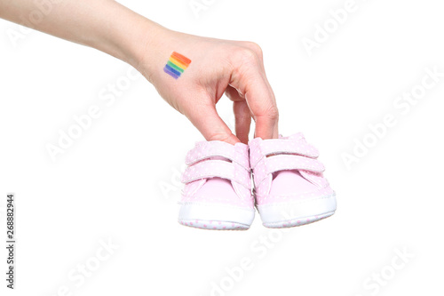 Female hand with drawing rainbow flag and baby shoes on white background