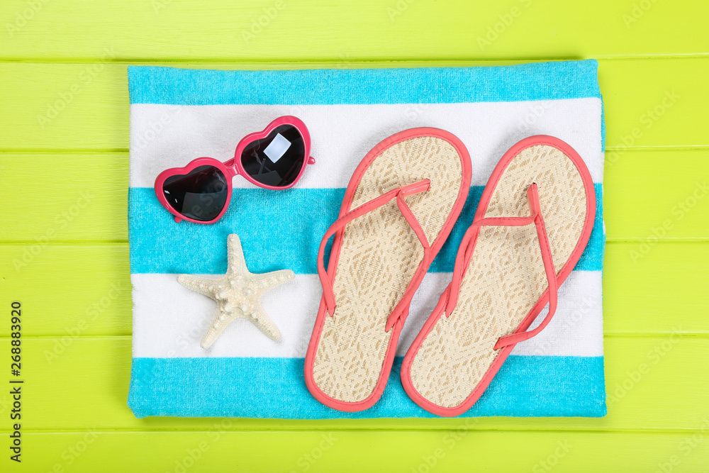 Fototapeta premium Pair of flip flops with starfish, towel and sunglasses on green wooden table