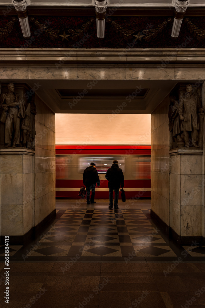 Passengers walking towards incoming red subway on the platform of Narvskaya metro station (Kirovsko-Vyborgskaya Line) (Saint Petersburg, Russia, Europe)