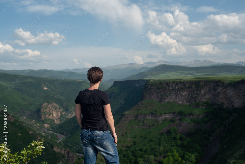 Naklejka premium The girl stands on the edge of a cliff and looks at the mountains. Armenia, Lori village. 