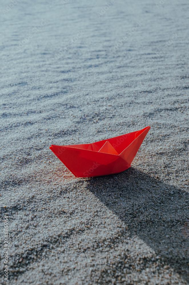 Red paper boat at the bottom of a dry sea. Beach, heat and vacation.Ecology, drought.
