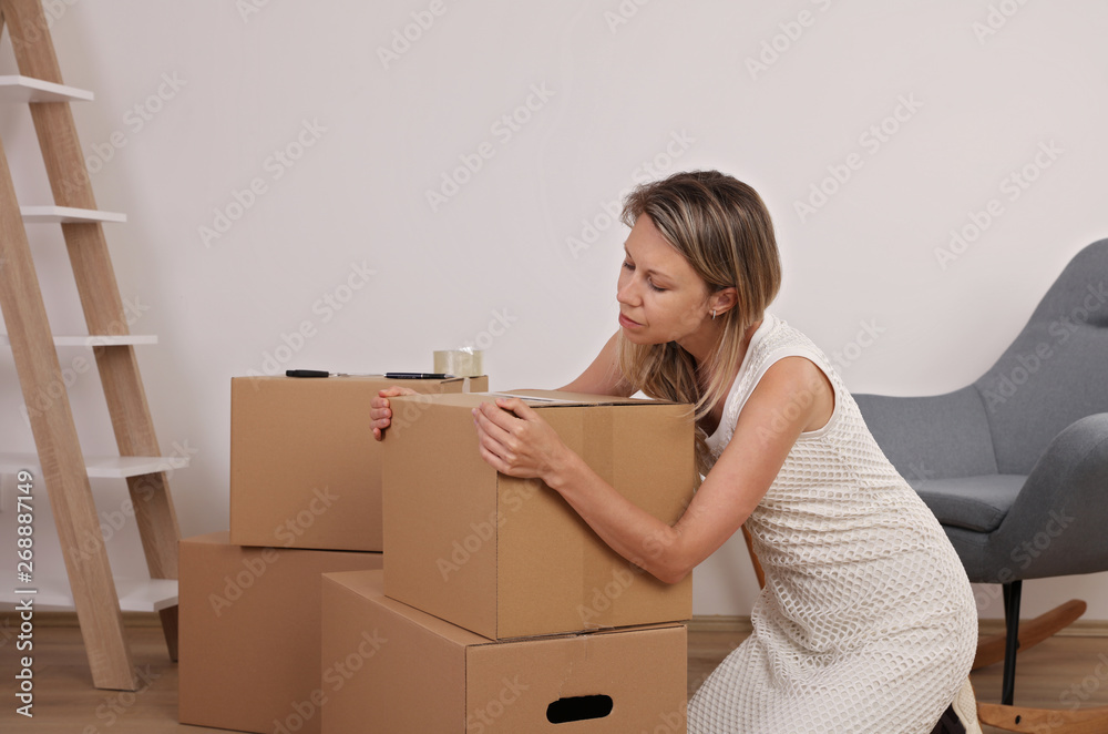 Moving in and out. Woman packing and labeling moving box at home
