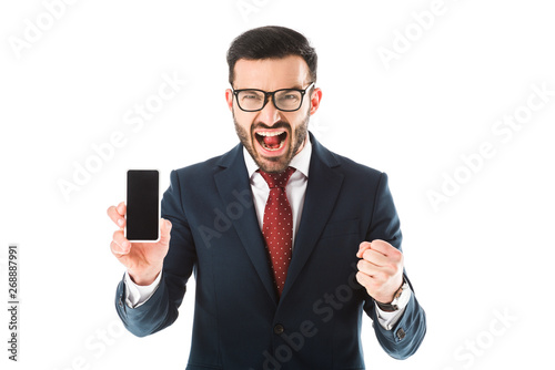 irritated businessman quarreling and showing fist while holding smartphone with blank screen and looking at camera isolated on white