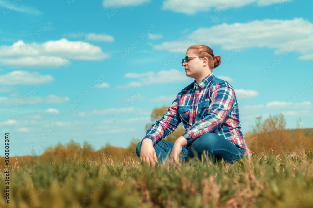 The guy sitting on the grass in a field on sky background. Copy space. The guy sitting on the grass in a field on sky background. Copy space.