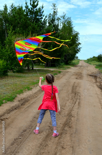 young girl in red dress running down the road with colour kite flying in the blue sky