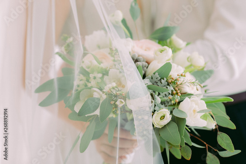 bride's hands hold beautiful bridal bouquet of white roses.